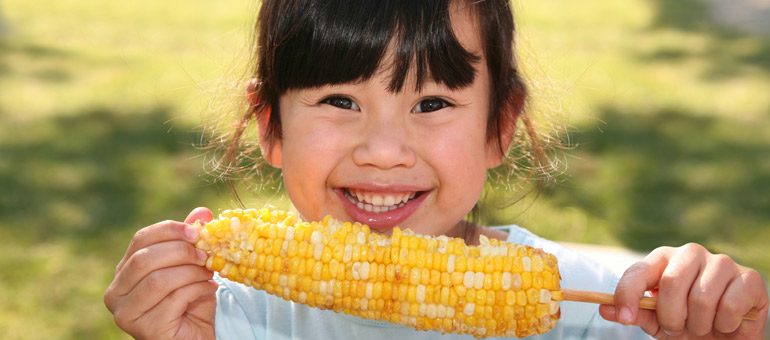 Une petite fille souriante qui mange du maïs